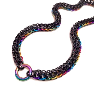 May include: A black chainmail necklace with rainbow detailing. The necklace is made of interlocking metal rings, with a rainbow-coloured clasp. The chainmail is black, with rainbow colours along the edges.