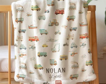 May include: A cream-colored baby blanket with a repeating pattern of various vehicles in muted colors. The blanket is draped over a wooden crib. The text "Nolan Lucas" is printed on the blanket.