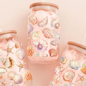 May include: Three glass mason jars with wooden lids and clear straws. Each jar is decorated with colorful seashells and starfish.