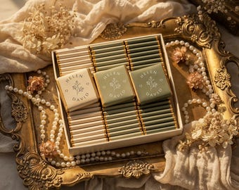 May include: A box of chocolates with personalized wrappers, featuring the names "HELEN DAVID" and a floral design. The chocolates are arranged on a gold-colored tray, surrounded by pearls and dried flowers, creating an elegant presentation.