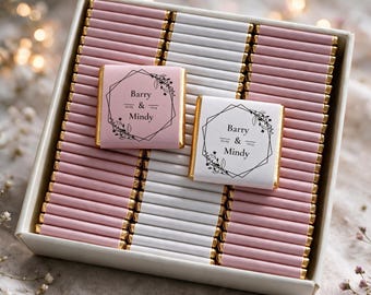 Puede incluir: Una caja cuadrada llena de filas de pequeñas barras de chocolate envueltas en papel aluminio rosa y blanco. Dos barras están colocadas encima, una rosa y otra blanca, cada una con un marco geométrico negro, detalles florales y el texto Barry & Mindy.