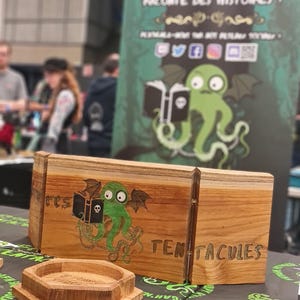 May include: Wooden box and ashtray set with a green octopus graphic and the word "TENTACULES". The box is made of light brown wood and has a hinged lid. The ashtray is hexagonal and also made of wood.