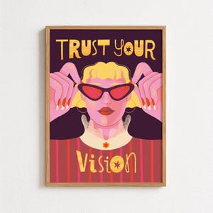 Könnte beinhalten: Ein gerahmter Kunstdruck mit einer stilisierten Illustration einer Frau mit roter Sonnenbrille. Das Kunstwerk trägt den Text "TRUST YOUR VISION" in Gelb. Die Frau hat blondes Haar und trägt ein rot-braun gestreiftes Oberteil.