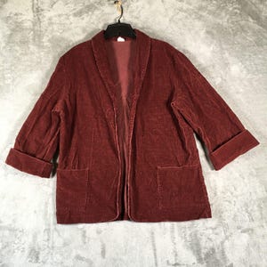 May include: A burgundy corduroy jacket with a shawl collar and two front pockets. The sleeves are cuffed at the elbow. The jacket is hanging on a black hanger.