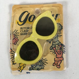 May include: Vintage yellow sunglasses with white polka dots, in original packaging. The sunglasses have dark lenses and a unique shape. The packaging features the word "Goofy" and the text "AUTOMATIC CLASP BARPETT".