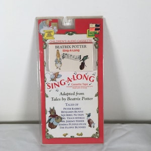 May include: A Beatrix Potter "Sing-A-Long" children's audio cassette tape. The packaging is red and white, with illustrations of Peter Rabbit and other characters. The cassette includes a fold-out lyric sheet with 25 songs. The package is sealed in clear plastic.