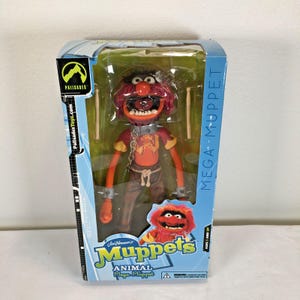 Puede incluir: Una figura de acción Animal de Mega Muppet de Palisades Toys en su empaque original. La figura tiene pelaje rojo, una boca ancha con dientes, un collar de púas con una cadena, una camisa naranja y pantalones marrones. Incluye dos baquetas.