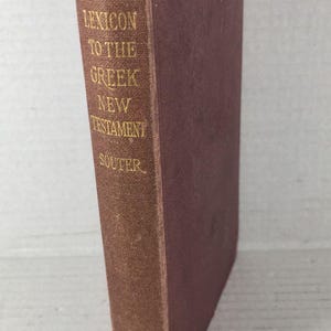 May include: A vintage book titled "A Pocket Lexicon to the Greek New Testament" by Souter. The book has a maroon cover with gold lettering and a gold emblem. The book is standing upright.
