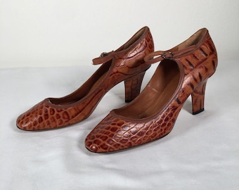 Op de afbeelding: Een paar bruine leren pumps met een textuurpatroon dat op reptielenleer lijkt. De schoenen hebben een vierkante neus, een bandje en een middelhoge hak. Het klassieke ontwerp heeft een bruine rand en een middelhoge hak.
