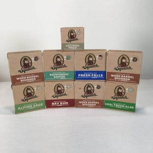 May include: A collection of nine Dr. Squatch natural soap bars in rectangular cardboard boxes. Each box features a cartoon sasquatch logo and specific scent names including Birchwood Breeze, Wood Barrel Bourbon, Rainforest Rapids, Fresh Falls, Alpine Sage, Bay Rum, and Cool Fresh Aloe.