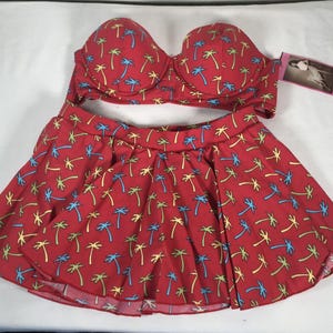Può includere: Costume da bagno a due pezzi rosso con motivo a palme. Il set comprende un top reggiseno senza spalline e un fondo a gonna. Le palme sono blu, gialle e verdi. L'etichetta recita "Belle Page".
