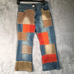Könnte beinhalten: Blaue Jeans mit einem Patchwork-Design mit rechteckigen braunen, beigen und orangefarbenen Paneelen. Die Jeans haben ein klassisches Fünf-Taschen-Design und einen geraden Bein-Schnitt. Der Patchwork-Look verleiht eine einzigartige, vom Vintage inspirierte Ästhetik.