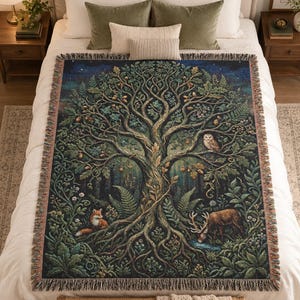 May include: A woven throw blanket featuring a detailed forest scene with a large central tree, a fox, a deer, and an owl. The design includes intricate branches, leaves, ferns, and flowers in shades of green, brown, and blue with a fringed edge.