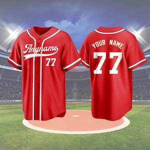 May include: Two red baseball jerseys with white accents. The front jersey has the text "Anyname" and the number "77". The back jersey has the text "Your Name" and the number "77". The jerseys are displayed on a baseball field.