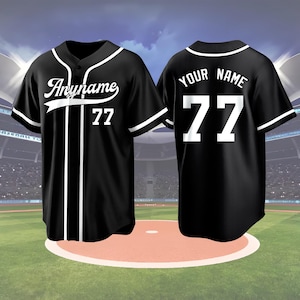 May include: Black baseball jersey with white accents, featuring the text "Anyname" and the number 77 on the front. The back of the jersey displays "YOUR NAME" and the number 77. The jersey has a button-up front and is set against a baseball field backdrop.