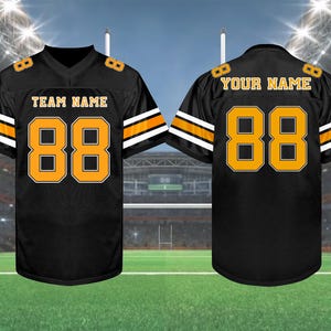 May include: Black football jersey with orange and white accents. The jersey features the number "88" in orange on the front and back, along with "TEAM NAME" and "YOUR NAME" in gold lettering. The jersey is displayed on a green field.