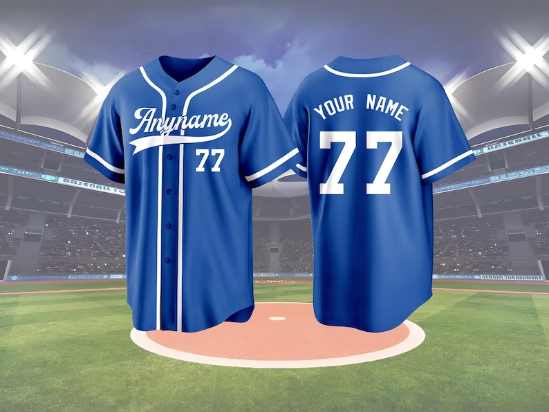 May include: A blue baseball jersey with white accents, featuring the text "Anyname" and the number 77 on the front. The back of the jersey displays "YOUR NAME" and the number 77. The jersey is displayed on a baseball field.