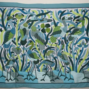 Puede incluir: Edredón hecho a mano con un diseño estilizado de garzas en tonos azules, verdes y blancos. Las aves se encuentran sobre un fondo de plantas y flores estilizadas, con un borde turquesa. Textil decorativo.