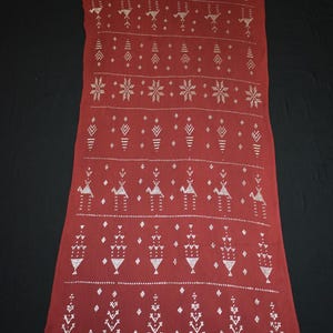 May include: A long, rectangular maroon textile with a repeating pattern of silver geometric shapes. The design includes rows of stylized arrows, diamonds, and starbursts. The textile is likely a scarf or shawl.
