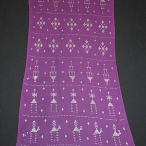 May include: A long, rectangular purple textile with a repeating pattern of stylized figures and geometric shapes in white. The design includes diamond shapes, dotted lines, and abstract human-like forms. The fabric appears to be a woven material.