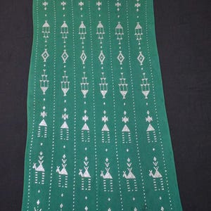 May include: Green textile with white geometric patterns. The design includes rows of stylized figures, diamonds, and arrows. The fabric has a soft texture and a dark green background.