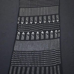 May include: Black and white patterned scarf with geometric designs. The scarf features alternating rows of dots, vertical lines, and zigzags. The edges are finished with small black tassels. The scarf is approximately 72 inches long.