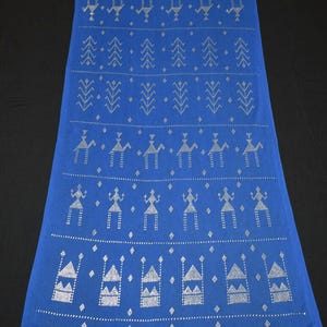 Puede incluir: Un textil azul largo y rectangular con un patrón repetitivo de figuras geométricas y humanas plateadas. El diseño incluye triángulos, flechas y figuras estilizadas, creando un patrón simétrico y decorativo.