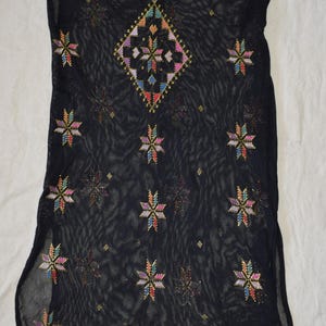 Puede incluir: Túnica negra transparente con patrones bordados de estrellas y diamantes coloridos. La túnica tiene cuello redondo y mangas cortas. El bordado presenta tonos de rosa, azul, amarillo y verde. La túnica probablemente está hecha de tela ligera.