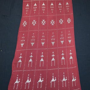 May include: A long, rectangular, burgundy textile with a repeating pattern of white geometric shapes and figures. The design includes rows of stylized figures, arrows, and diamond shapes, creating a symmetrical and decorative pattern.