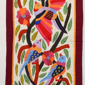 May include: A rectangular wall hanging featuring colorful fabric appliqué of birds, flowers, and leaves on a cream background. The design includes multiple birds in shades of orange, blue, and pink perched on dark branches, framed by a deep red border.
