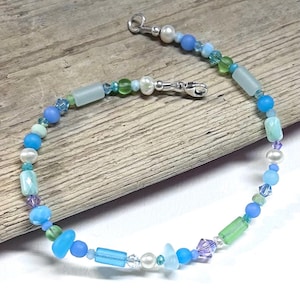 May include: A beaded bracelet featuring a variety of blue, green, and white beads, including frosted glass cylinders, round matte beads, faceted crystals, and small white pearls. The bracelet is secured with a silver-toned metal lobster clasp.