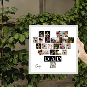 May include: A white framed photo collage in the shape of a heart, filled with multiple small photos. The word "DAD" is displayed in black block letters, with the name "Emily" in cursive below. The background features green foliage.