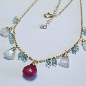 May include: A gold chain necklace with a large red gemstone pendant and smaller blue and white gemstones hanging from the chain.
