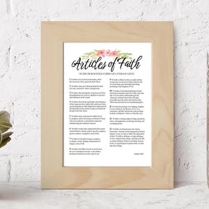 May include: A framed print with a white background and a floral design at the top. The text "Articles of Faith" is in black lettering. The text below reads "Of The Church of Jesus Christ of Latter-day Saints". The text is in black and white and lists the 13 articles of faith.