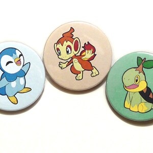 May include: Three round buttons with cartoon Pokemon characters. The first button is light blue with a blue and white penguin. The second button is light brown with a red and yellow monkey. The third button is green with a green and yellow turtle.