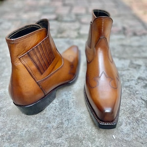May include: A pair of brown leather ankle boots with a pointed toe and decorative stitching. The boots have a pull-on design with elastic side panels and a stacked heel.