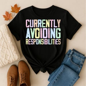 May include: A black short-sleeved t-shirt featuring the text "CURRENTLY AVOIDING RESPONSIBILITIES" in a distressed, multi-colored pastel font. The letters are printed in shades of pink, yellow, green, and blue against the dark fabric.