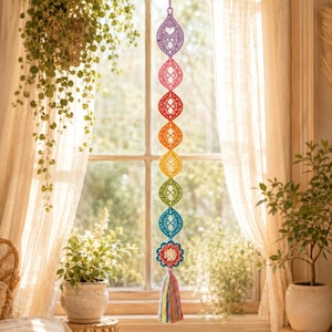 May include: A vertical hanging decoration featuring a series of eight connected crochet ornaments in a rainbow color gradient, starting with purple at the top and ending with a multi-colored flower and a long, thin, multicolored yarn tassel.