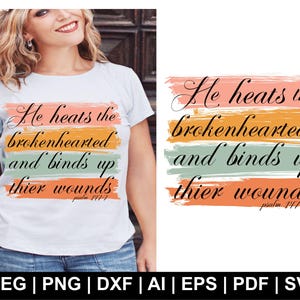 Può includere: T-shirt bianco con la scritta "He heats the brokenhearted and binds up thier wounds" in corsivo nero. Il testo è sovrapposto a pennellate orizzontali rosa, arancioni, verdi e arancioni. Un capo casual.