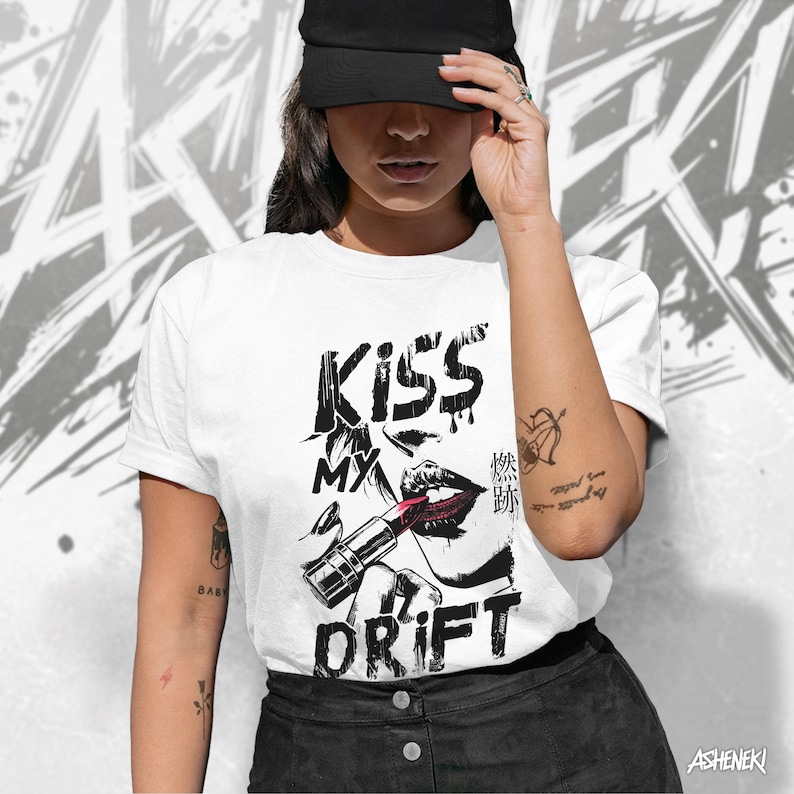 May include: A white t-shirt with a black and white graphic design of a woman's lips with lipstick and the text "Kiss My Drift".