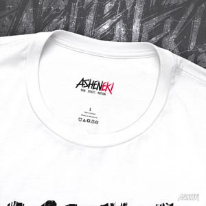 May include: White t-shirt with a black and red graphic print of the word "ASHENEKI" and the text "RAW, STREET, MOTION". The shirt has a tag that says "100% Cotton" and "Made in Honduras".