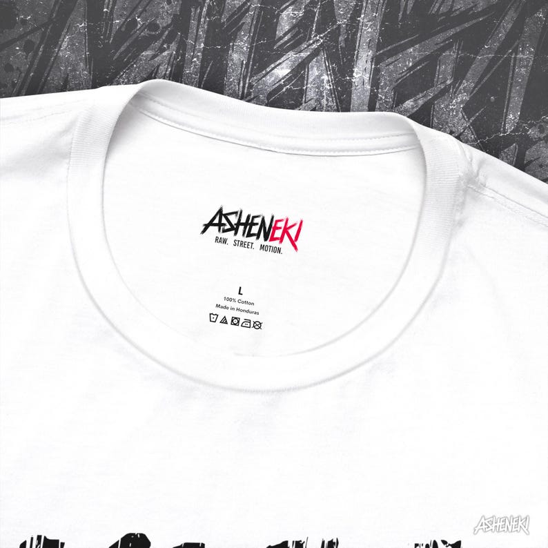 May include: White t-shirt with a black and red graphic print of the word "ASHENEKI" and the text "RAW, STREET, MOTION". The shirt has a tag that says "100% Cotton" and "Made in Honduras".