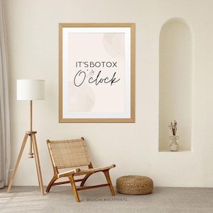 May include: A framed print with a light pink background and the text "IT'S BOTOX O'clock" in black. The print is hanging on a white wall with a wooden frame.