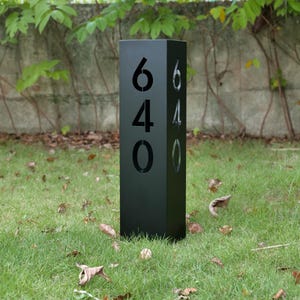 May include: A black address post with the numbers 640 cut out on the front and side. The post is rectangular and stands on a grassy lawn. The numbers are large and easy to read.