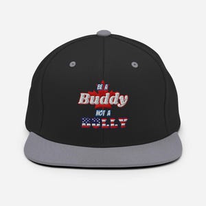 Puede incluir: Gorra de béisbol negra y gris con un diseño bordado en rojo, blanco y azul que dice "Be a Buddy Not a Bully".