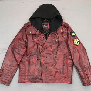 May include: A distressed red leather jacket with a black hood. The jacket features a quilted design on the shoulders and lower front, multiple zippers, and decorative patches. The jacket has the text "Real Leather" on a tag.