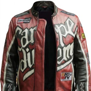 Puede incluir: Una chaqueta de cuero roja y negra con letras y parches blancos. La chaqueta presenta las palabras "Car Di" y "Pe Em" en letras blancas grandes. Los parches incluyen "Champion" y "K&N".