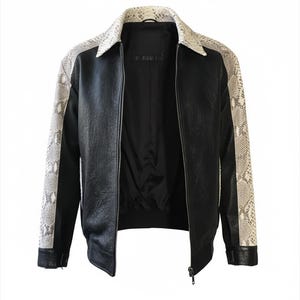 May include: Black jacket with a snakeskin pattern on the sleeves and collar. The jacket has a zipper closure and a black interior lining. The sleeves and collar feature a cream and gray snakeskin print, contrasting with the black body of the jacket.