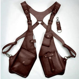 Pode incluir: Coldre de ombro em couro marrom com vários bolsos e alças ajustáveis. Inclui um porta-chaves a condizer. O coldre foi concebido para ser usado no peito e nas costas, com bolsos para transportar objetos.