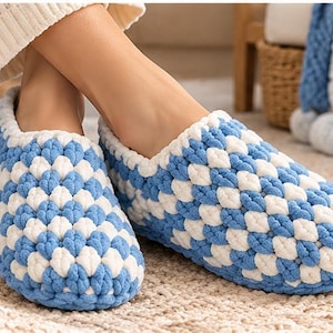 May include: A pair of handmade crochet slippers featuring a textured, puffy stitch pattern in alternating blocks of light blue and white yarn. The slippers have a rounded toe design and a thick, soft construction that covers the entire foot.